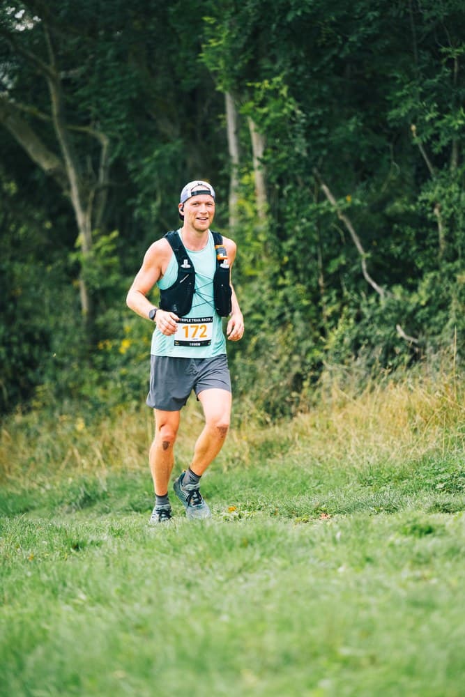 Sven running through a forest wearing a race bib at a trail ultra